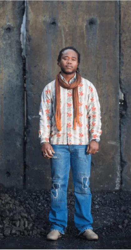 Belondjo Bolankoko, fondateur et mentor de DesignLab Academy, debout devant un mur de béton.